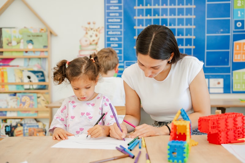 Adult helping a young child with drawing at a classroom table